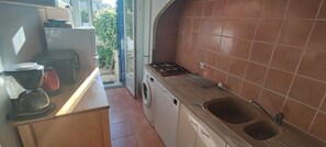 Cocina pequeña con lavadora, un lavabo y ventana que da a un jardín.