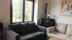 A living room with a grey sofa, a beige sofa, a wooden coffee table, a bookshelf, and a window with blinds.