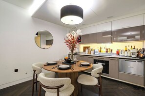A modern kitchen with a round dining table, chairs, and a central vase with flowers. - Luxury Covent Garden 2-Bed, 3-Bath+Balcony for 4 (London)