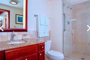 Ein Badezimmer mit einer Waschtilfe aus Granit, einem roten Waschtischunterschrank, einer weißen Toilette, einer Duschkabine aus Glas und einem großen Spiegel.