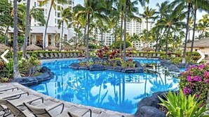 Zwembadcomplex van een resort met ligbedden, palmbomen en een helderblauw zwembad omringd door rotsen en tropische planten.