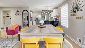 A modern kitchen with a central island, a dining area with a wooden table and yellow chairs, and a living space with a pink chair and a decorative mirror. - Private Pickleball Court+Huge Fenced Yard, Easy Access to Grand Park & Downtown (Indianapolis)