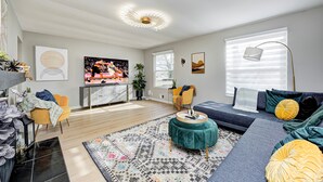 A modern living room with a sofa, armchair, and ottoman, a coffee table, a TV, and a decorative ceiling light. - Private Pickleball Court+Huge Fenced Yard, Easy Access to Grand Park & Downtown (Indianapolis)