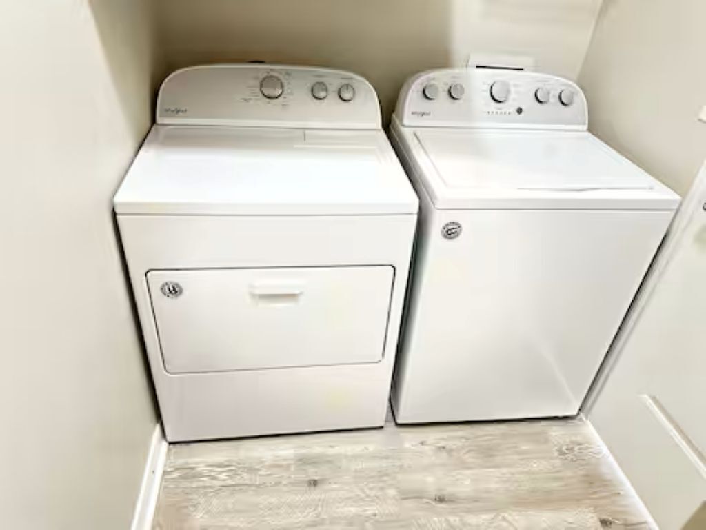 Two white front-loading washing machines in a laundry room with a wooden floor.