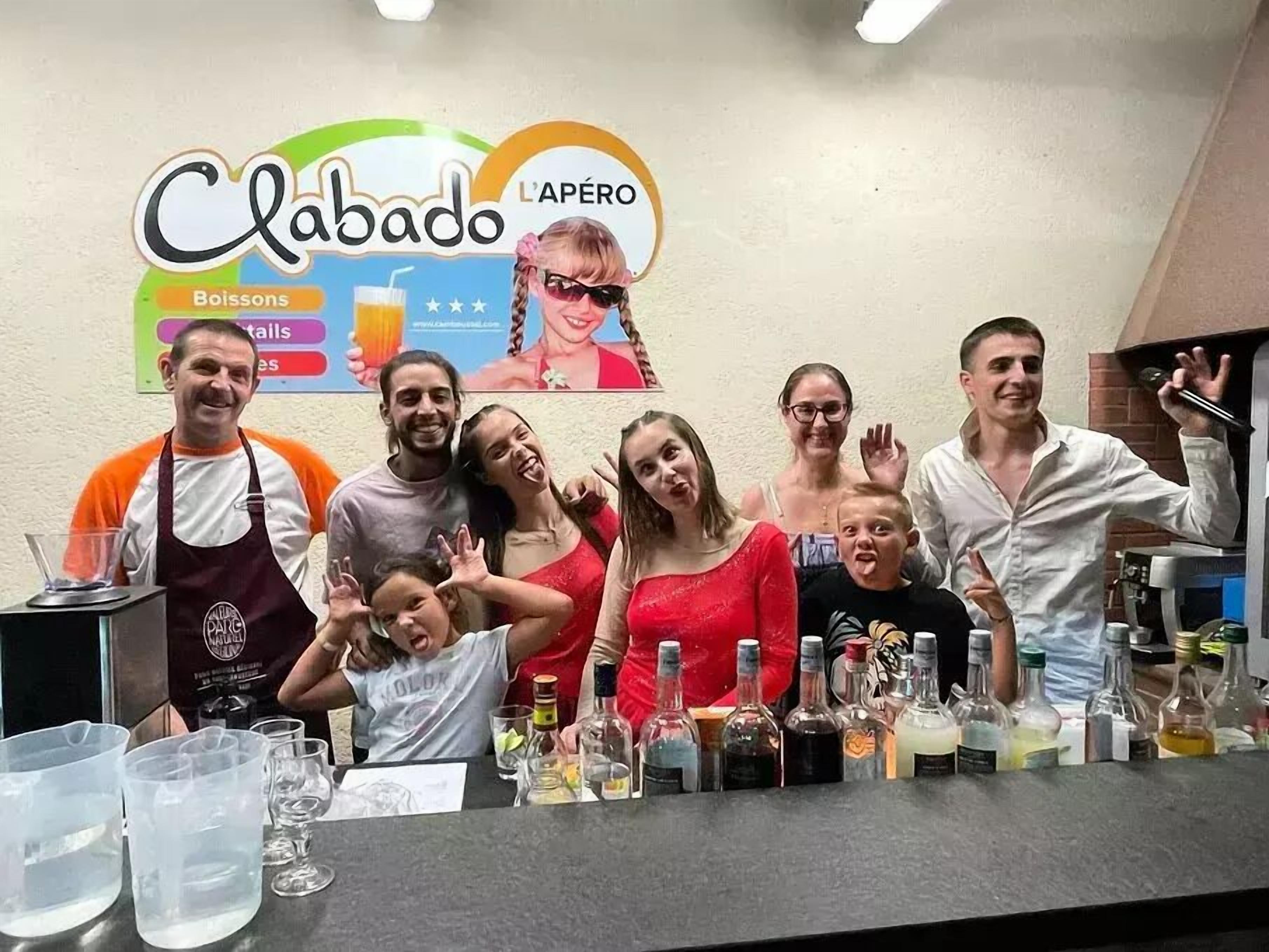 A group of people posing in front of a bar with a sign that reads "Clabado L'APÉRO".