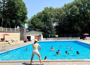 Ein Pool mit darin badenden Personen, umgeben von Bäumen und einem Gebäude mit weißer Fassade.