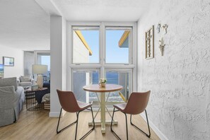 Ein modernes Wohnzimmer mit einem runden Tisch, zwei Stühlen, einer Couch und Meerblick durch große Fenster.