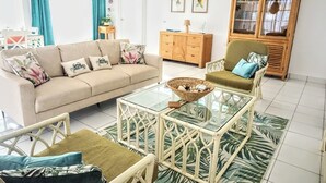 A living room with a beige sofa, a glass coffee table, wicker chairs, a wooden cabinet, and a patterned rug. - Cas Pega Pega - Close To Beach - Centrally Located (Paradera)