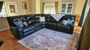 Un salon comprenant un canapé d’angle en cuir noir, un tapis à motifs et un meuble contenant des objets décoratifs.
