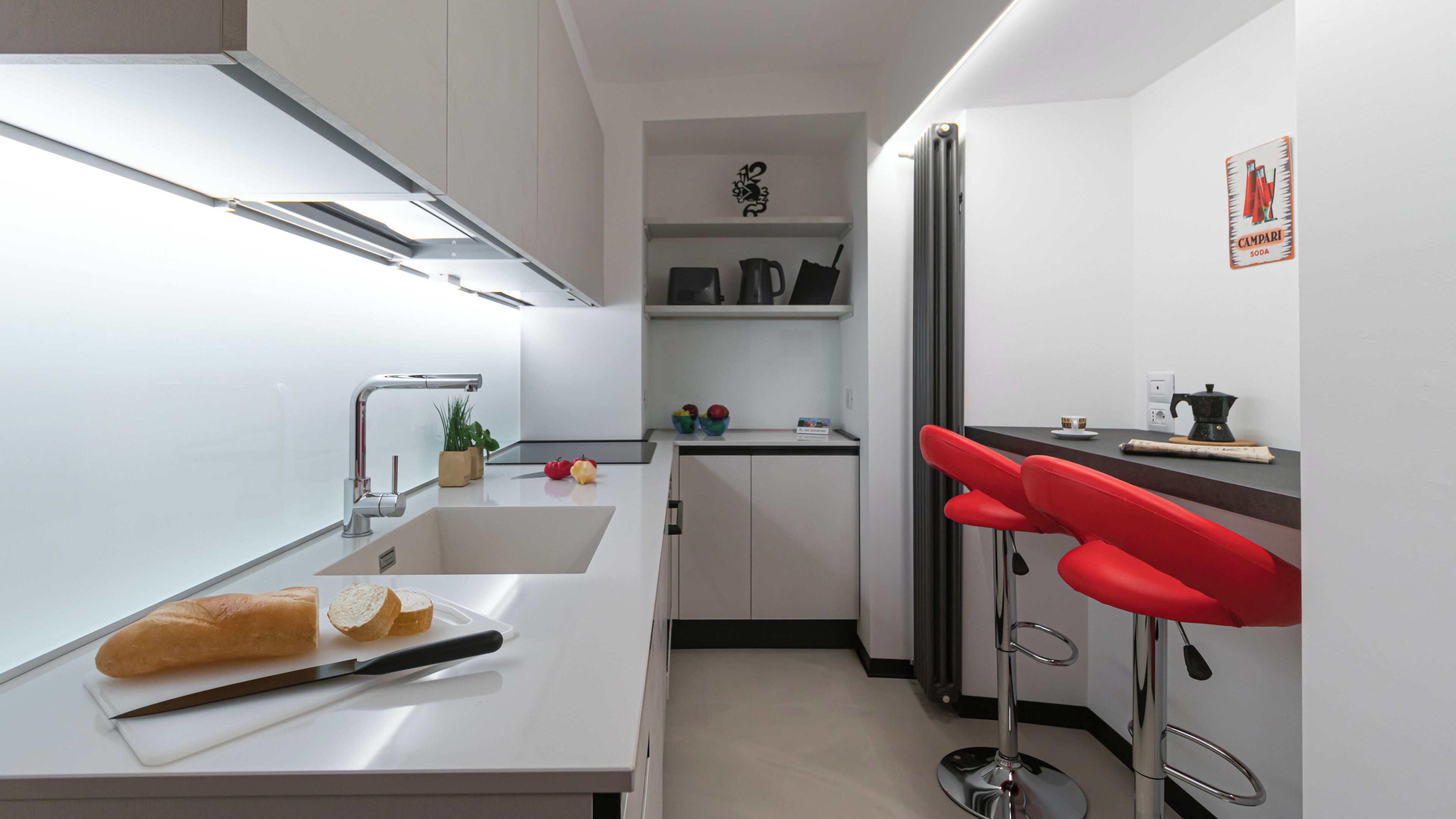 A modern kitchen with a sink, cutting board, and red bar stools.