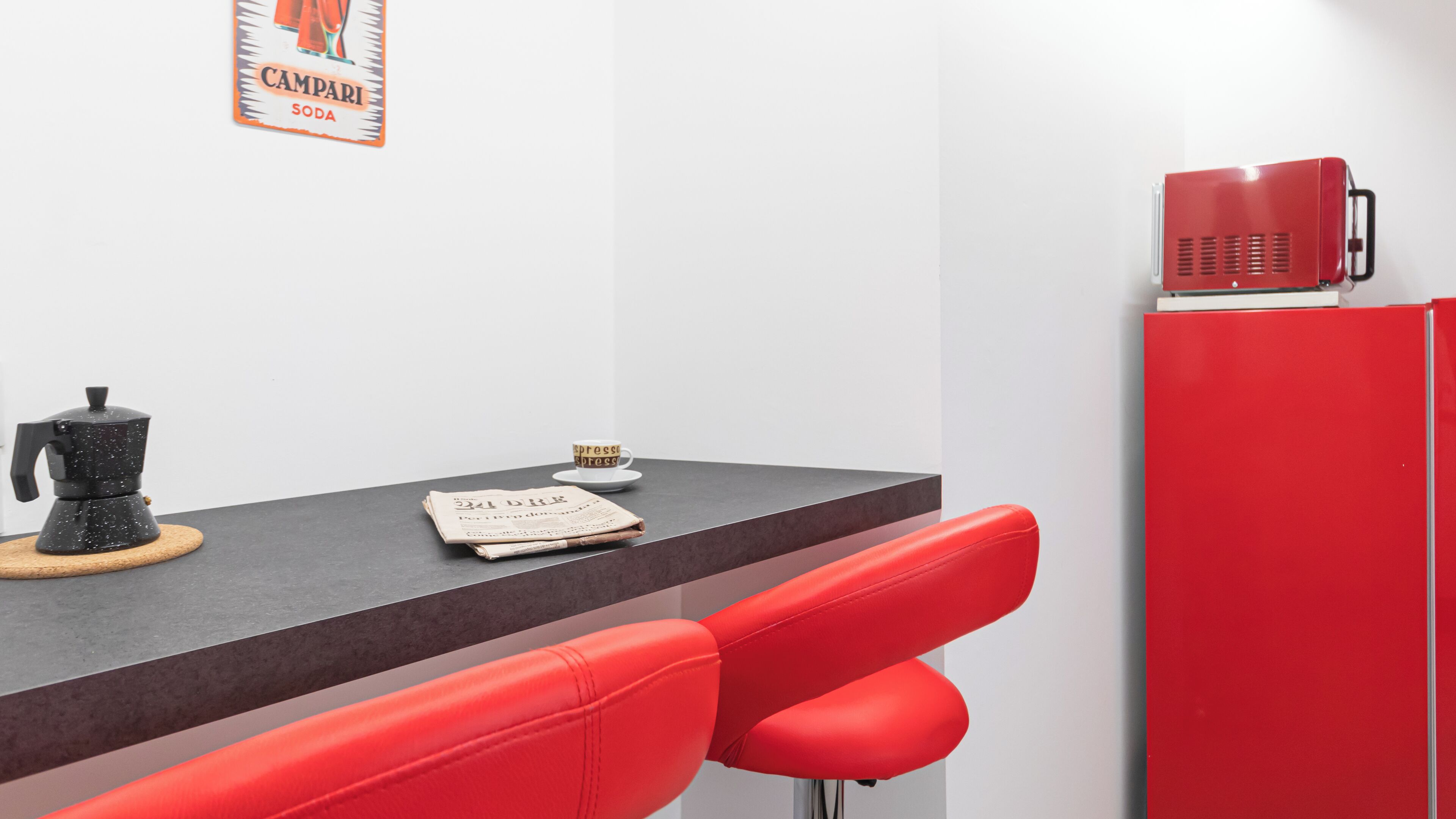 A modern kitchen with a coffee machine, a newspaper, and a red refrigerator.