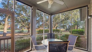 Un porche cubierto con una mesa y sillas de vidrio, con vista a un jardín ajardinado y árboles.