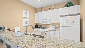 Una cocina moderna con gabinetes blancos, encimeras de granito, microondas, estufa y refrigerador.