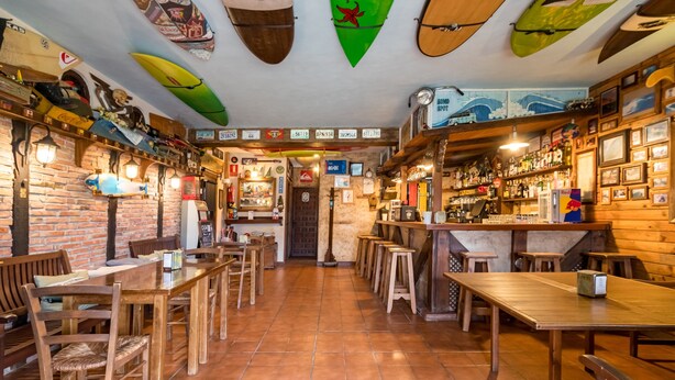 A bar with wooden furniture, surfboards on the ceiling, and a brick wall.