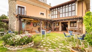 A building with a stone facade, a covered patio with outdoor seating, and a garden area with flowers.