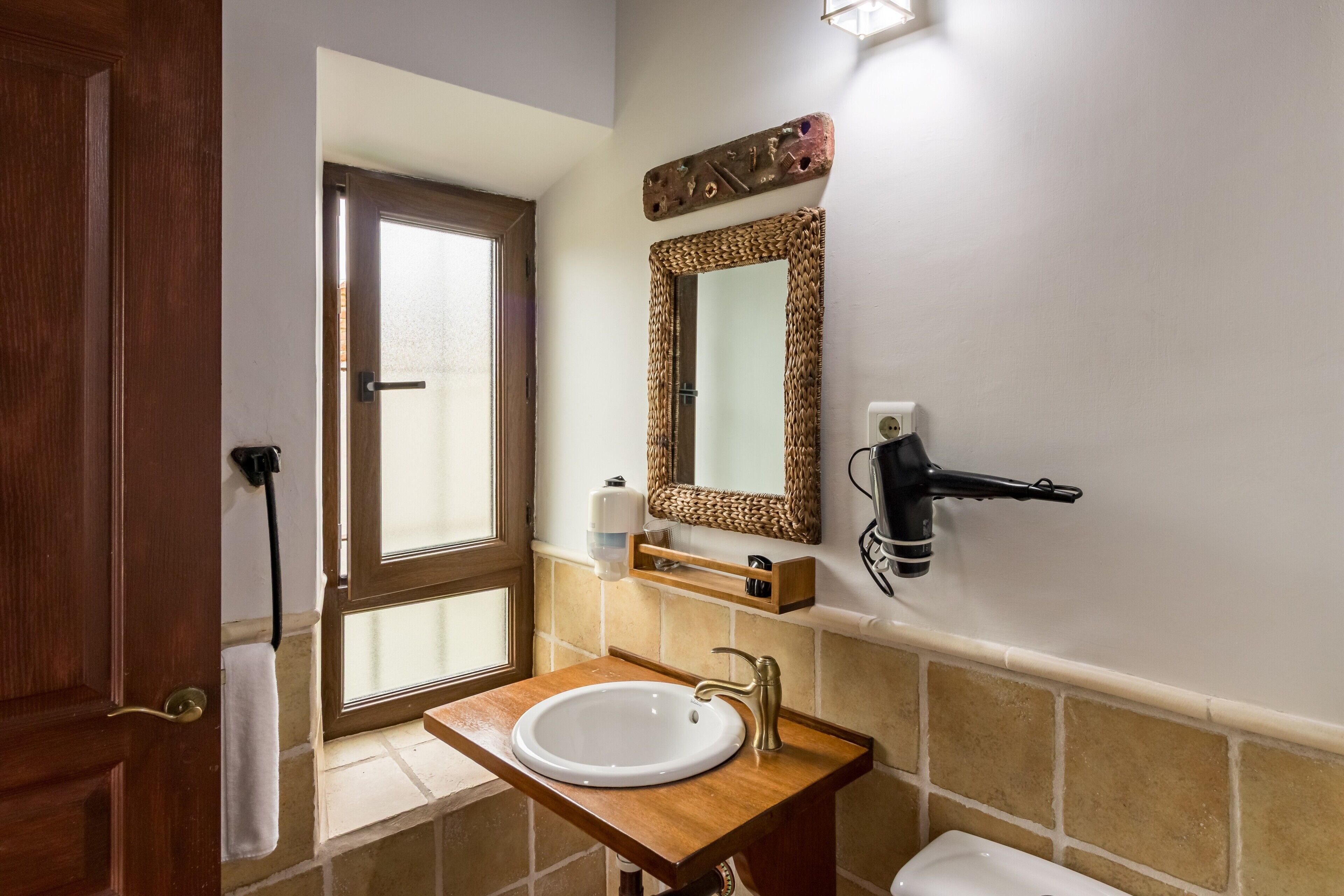 A bathroom with a wooden vanity, a white sink, a mirror, and a towel hanging on the door.