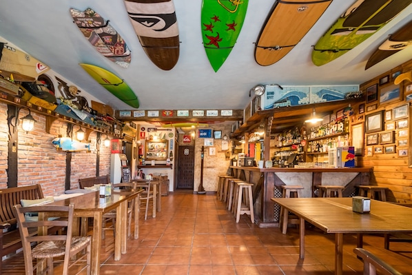 A bar with wooden furniture, surfboards on the ceiling, and a brick wall.