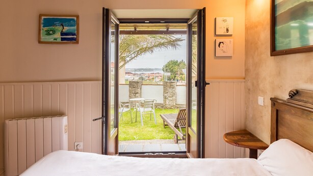 Ein Schlafzimmer mit Bett, einem kleinen Tisch, einem Sessel und einem Fenster mit Blick hinaus.