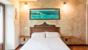 Ein Schlafzimmer mit einem hölzernen Kopfteil, einem Bett mit weißer Bettwäsche, zwei Nachttischen, einem gerahmten Bild von einer Strandlandschaft und zwei Wandleuchten.