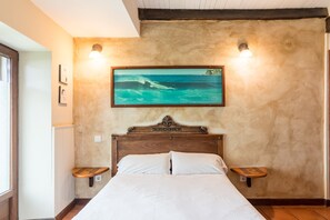 A bedroom with a wooden headboard, a bed with white bedding, two bedside tables, a framed picture of a beach scene, and two wall-mounted lights. - Casa Del Surf Somo: Room 4 with Sea Views and Private Garden (Somo)