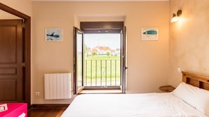Ein Schlafzimmer mit einem Bett, einer Tür, die auf einen Balkon führt, einem Heizkörper und zwei an der Wand befestigten Kunstwerken.