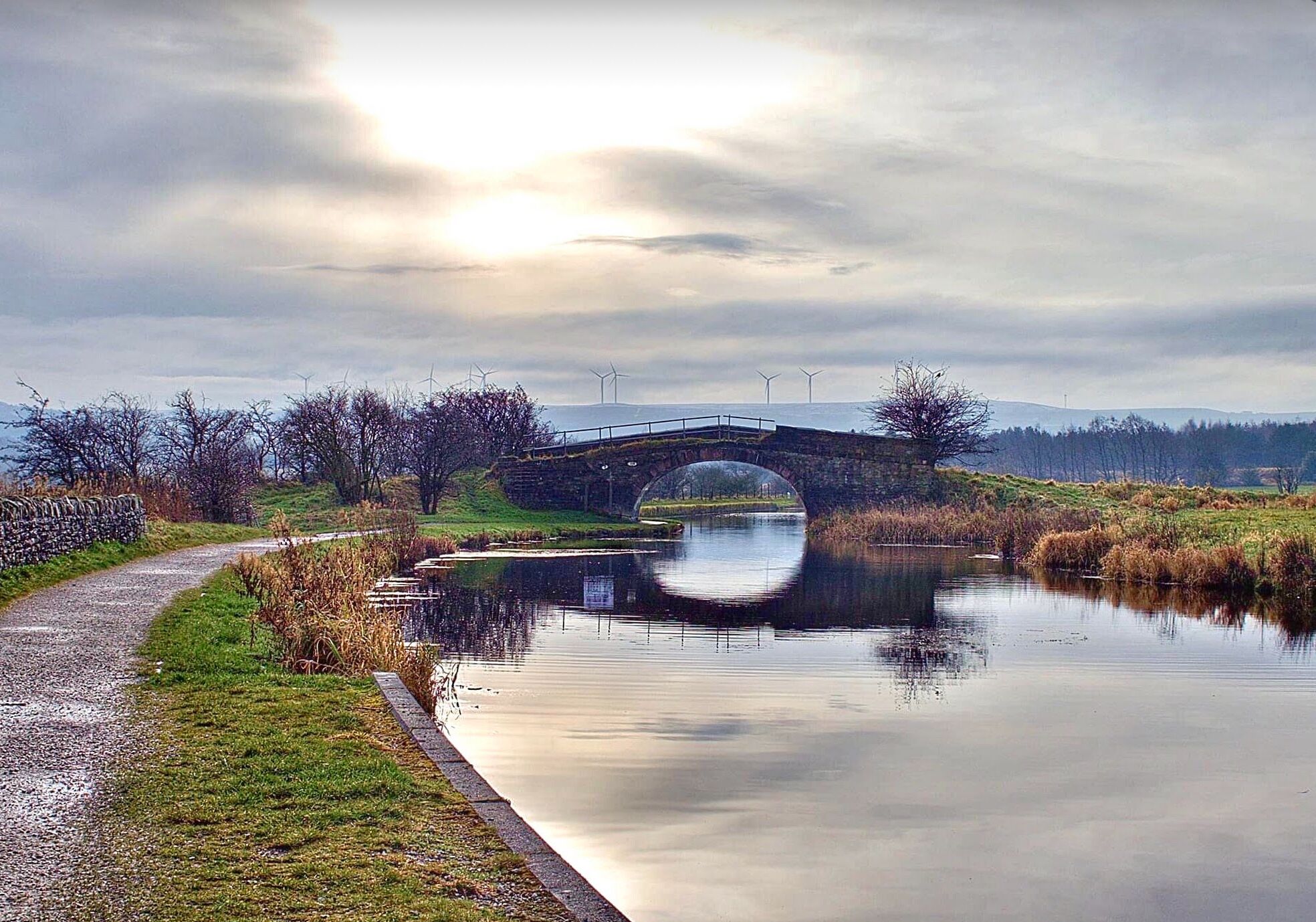 Eine Steinsche Brücke überspannt einen ruhigen Fluss, umgeben von grasbewachsenen Ufern und Bäumen.