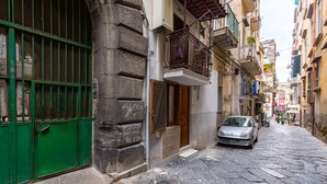 Una estrecha calle adoquinada con una verja metálica verde, un coche aparcado, y edificios con balcones y ventanas.
