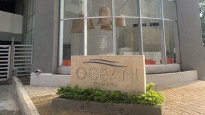 A modern building with a large glass facade, a sign reading "OCEANI TOWERS," and a small garden area with plants.