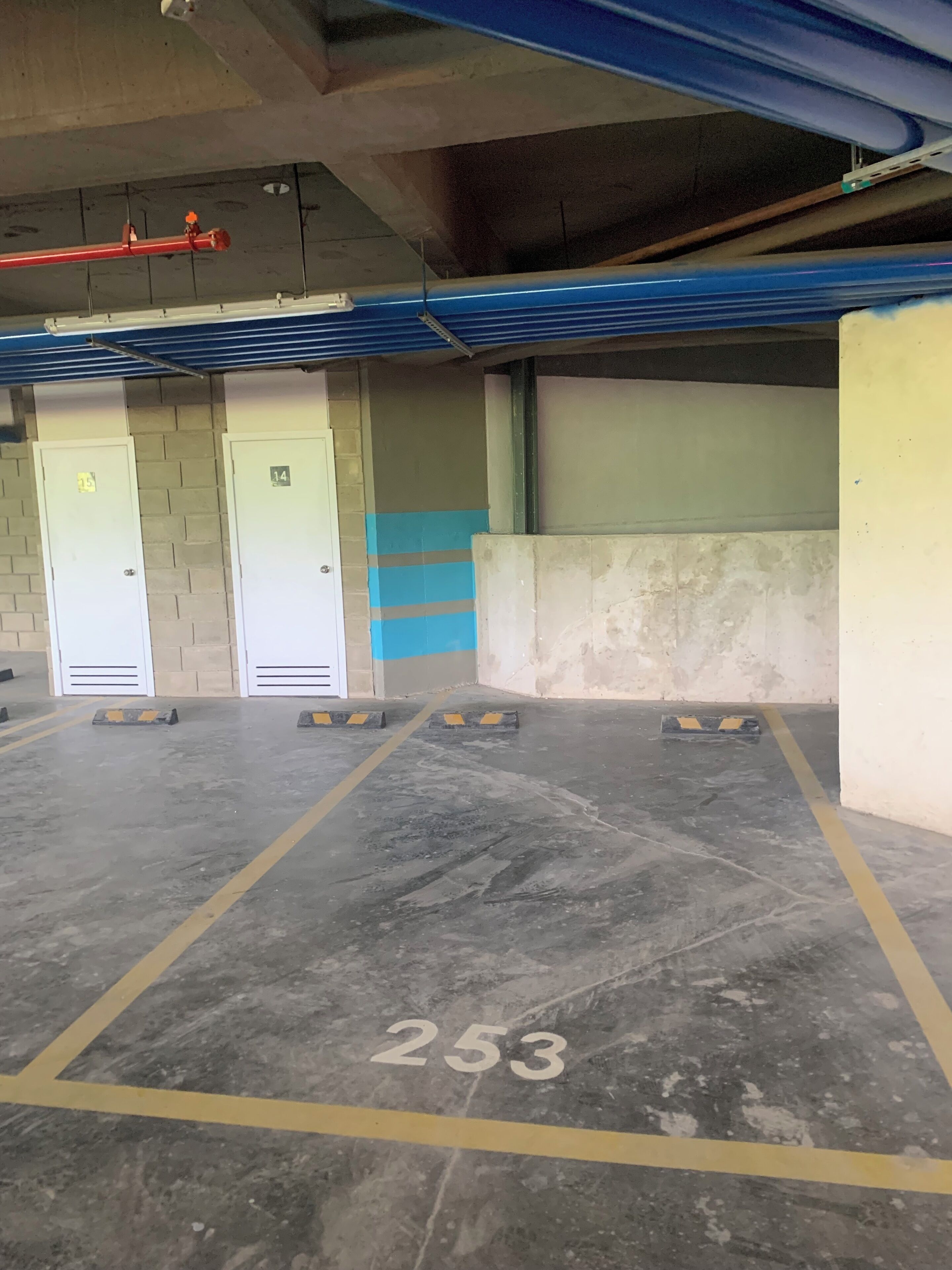 Ett parkeringsgarage med numrerade parkeringsplatser, inklusive plats nummer 253, och en blå och beige vägg med en dörr märkt med nummer 14.