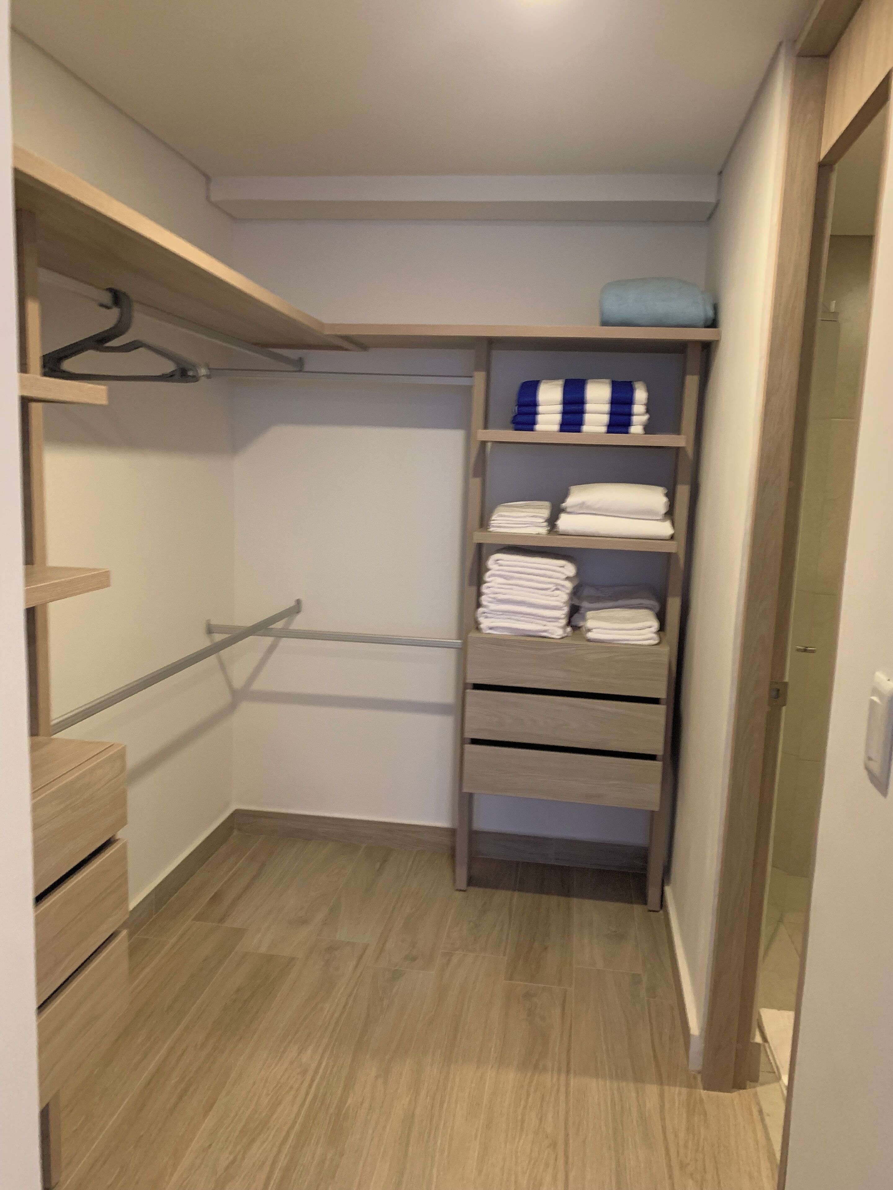 A walk-in closet with wooden shelves, a hanging rod, and a blue towel on the top shelf.