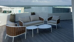 Et moderne udendørs opholdsområde med sofa og stole, et lille bord og havudsigt.