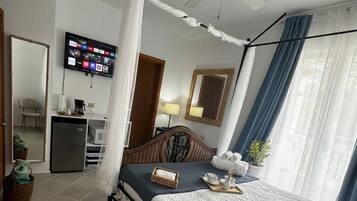 Une chambre à coucher avec un lit à baldaquin, un ventilateur de plafond, un téléviseur fixé au mur et un bureau équipé d’un ordinateur et d’une lampe.