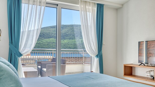 A hotel room with a bed, a TV, and a balcony with a view of a hillside. - Apartments Ljubica  (Denovici)