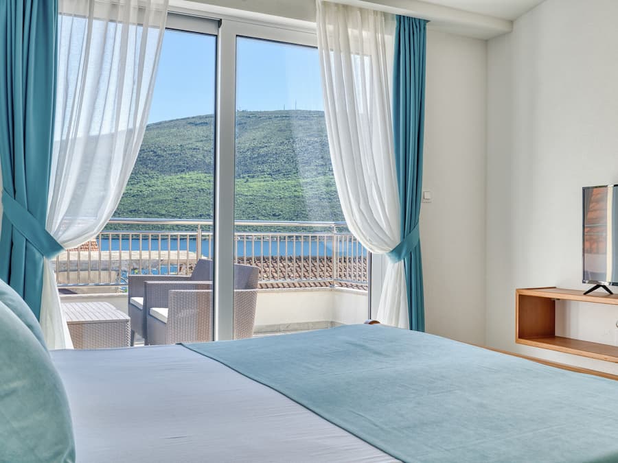 A hotel room with a bed, a TV, and a balcony with a view of a hillside.