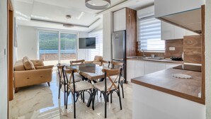 A modern kitchen with a central island, a dining area with a glass-top table, and a living area with a sofa and TV. - Apartments Ljubica  (Denovici)