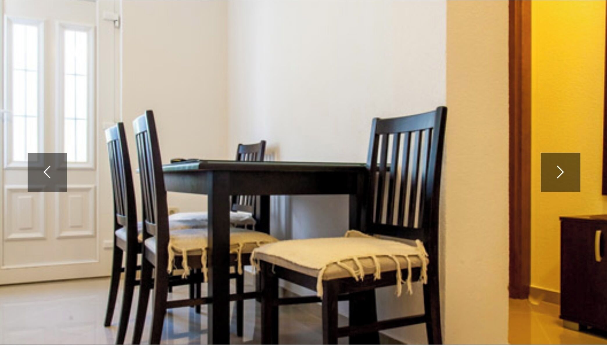 A dining area with a dark wooden table and four chairs, each with a light-colored cushion.