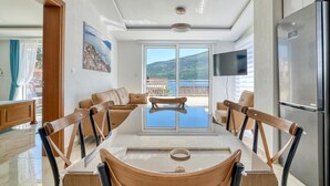 A modern dining area with a glass table, wooden chairs, and a view of a mountainous landscape through large windows. - Apartments Ljubica  (Denovici)