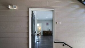 Een gang met een deur naar een kamer. De gang heeft een lichtgekleurde muur en een donkere vloer. Op de muur staat het nummer '423'.