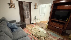 Ett vardagsrum med en grå soffa, ett soffbord, ett TV-bord och en mönstrad matta.