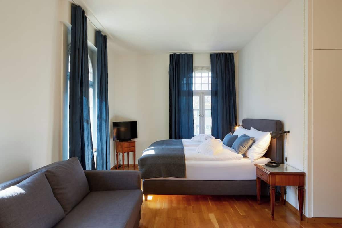 A bedroom with a bed, a TV on a side table, and a sofa.