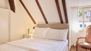 Ein Schlafzimmer mit Bett, Holzbalken, einem Nachttisch und einem Sessel.