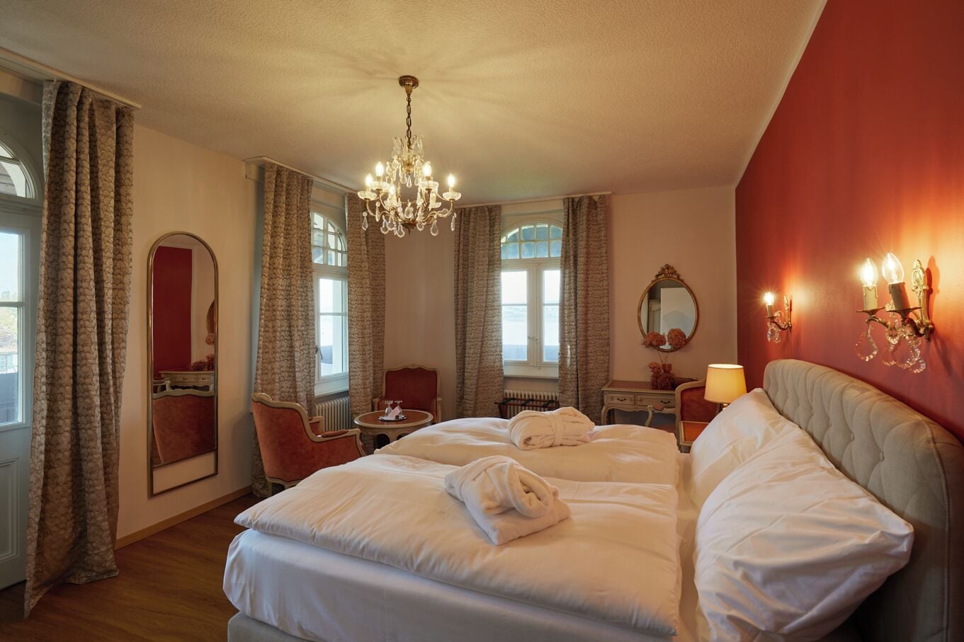 Une chambre d’hôtel avec un grand lit, un coin salon comprenant une chaise et une table, un miroir et un lustre.