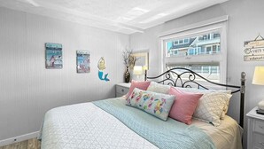 A bedroom with a bed, a nightstand, a window, and wall decorations. - Admiral's Quarters (Wells)