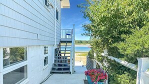 A white building with a covered outdoor area leading to a pool, surrounded by greenery and a clear view of the beach. - Admiral's Quarters (Wells)