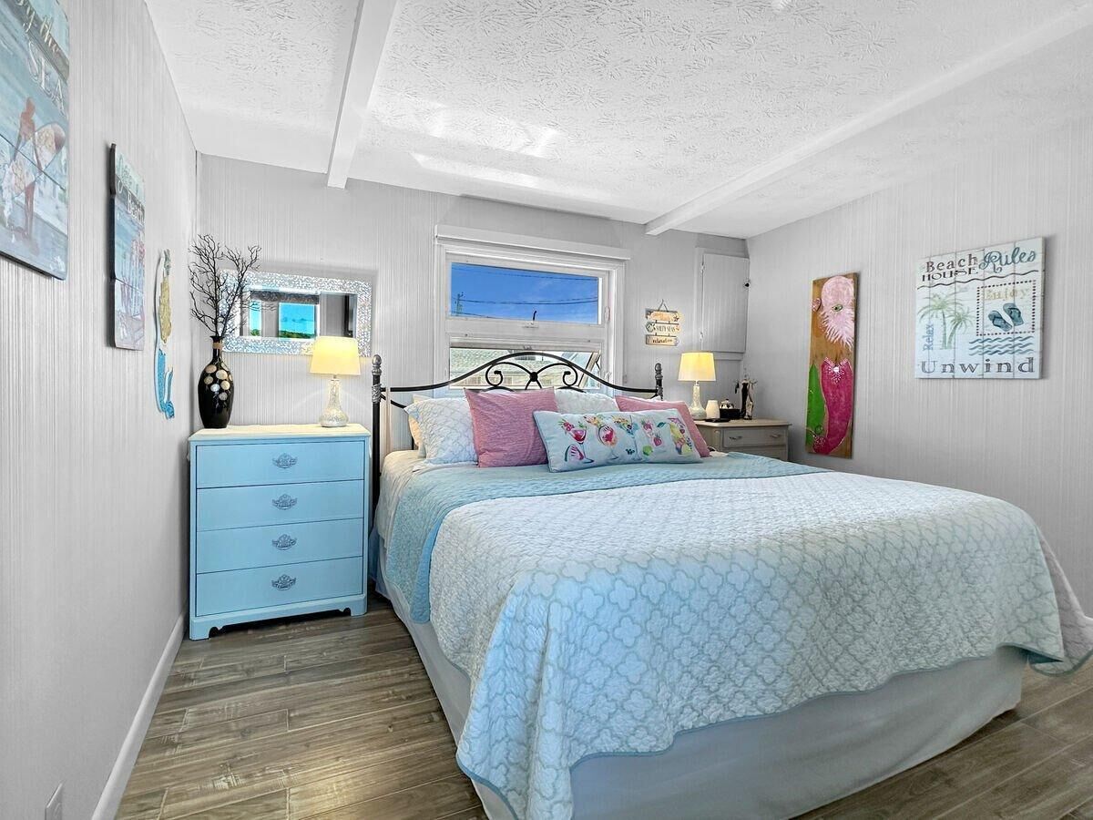 A bedroom with a bed, a nightstand, a dresser, a window, and wall art.