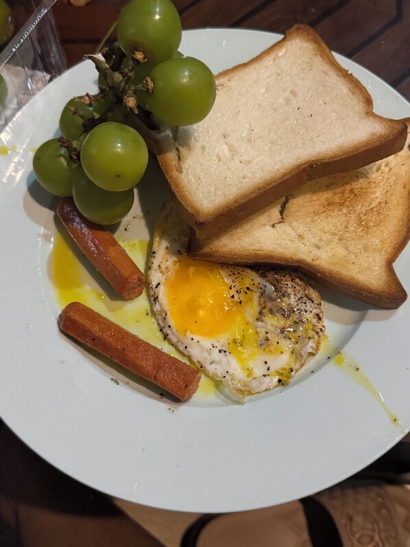 A plate with a fried egg, toast, sausages, and grapes.