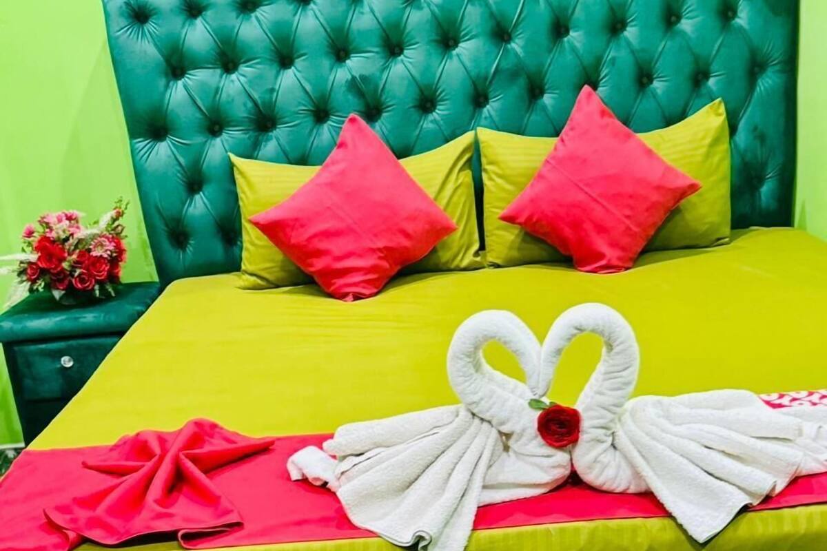 A bed with a green upholstered headboard and a bright yellow bedspread. There are two red pillows and a bouquet of flowers on the nightstand beside the bed.