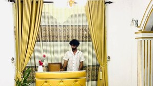 A reception area with a yellow tufted desk, a potted plant, and curtains.
