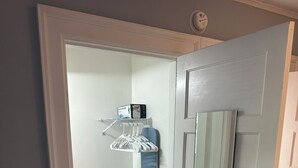 Un couloir avec une porte blanche, une étagère bleue fixée au mur avec une boîte dessus, et un miroir.