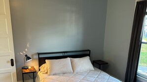 Une chambre avec un grand lit, une table de chevet avec une lampe et une fenêtre avec des rideaux.
